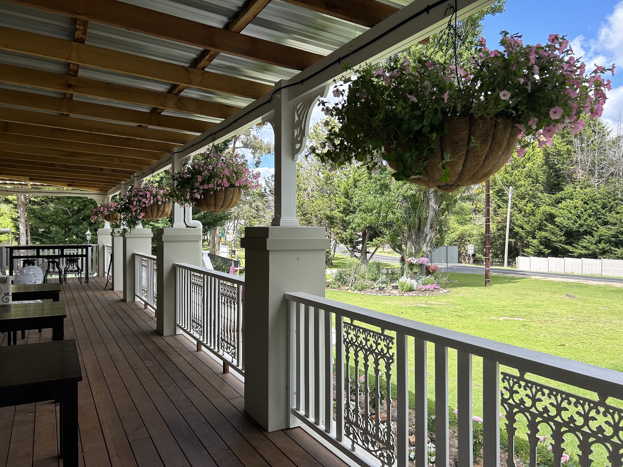 The long timber veranda with lace-iron railings, flower baskets and tables looking over the lawn