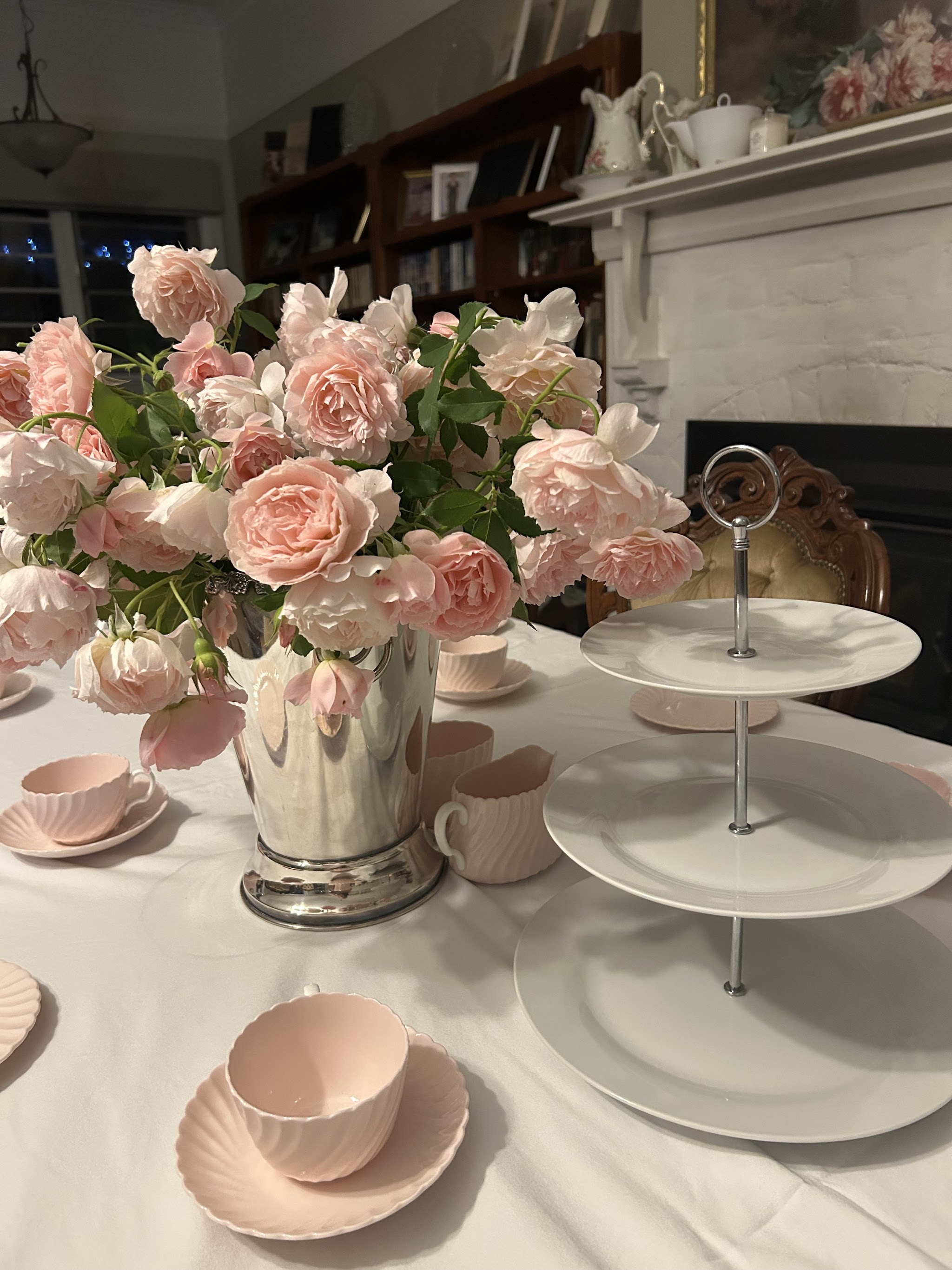 High tea table with fine china, a tiered cake stand and roses by the fireplace