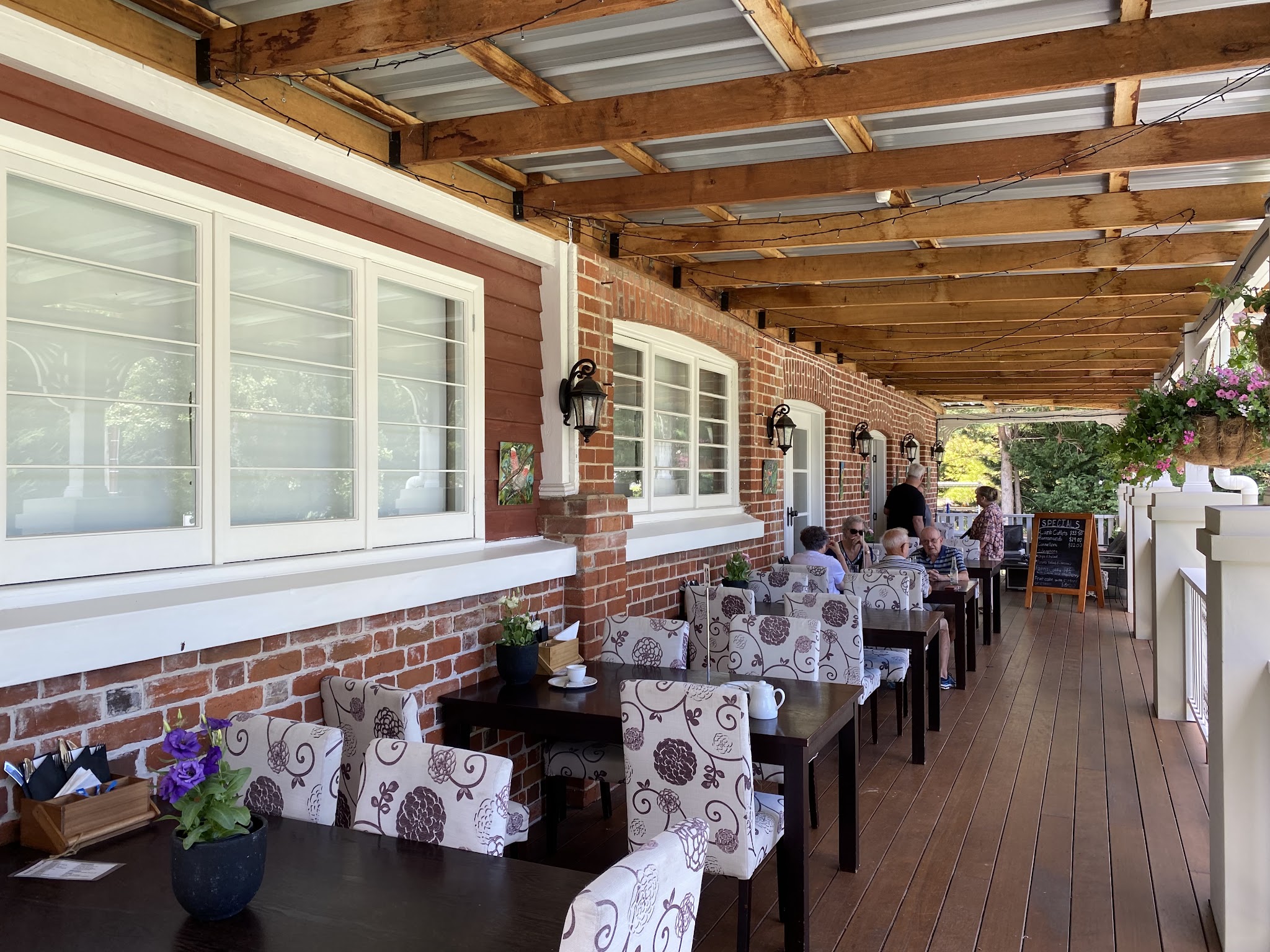 Guests dining on the veranda under fairy lights beside the specials board