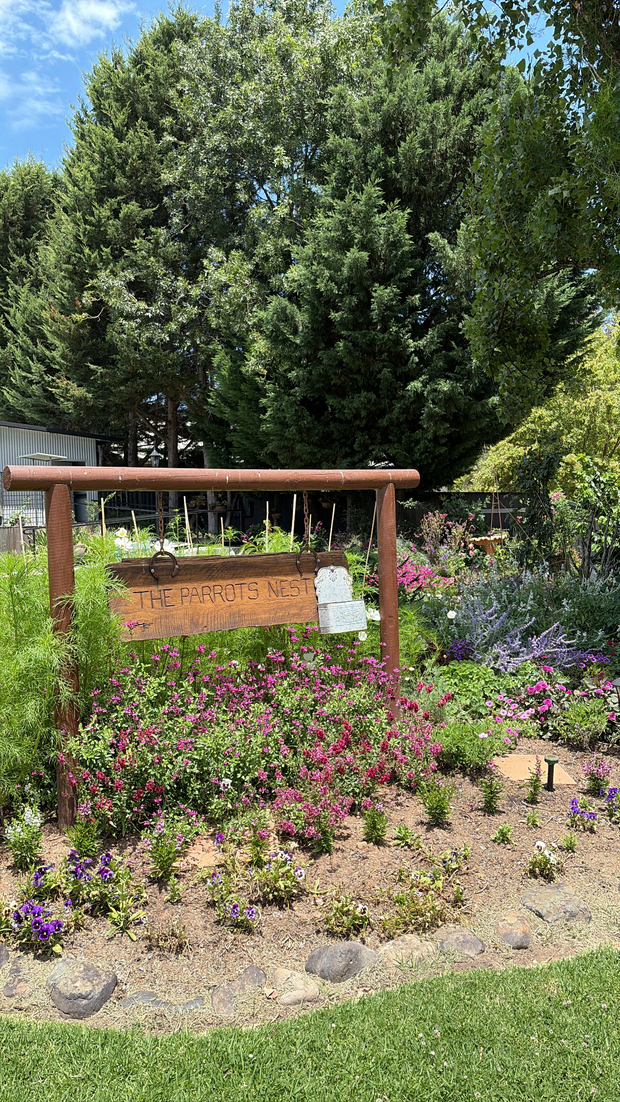 The Parrots Nest garden sign surrounded by flower beds