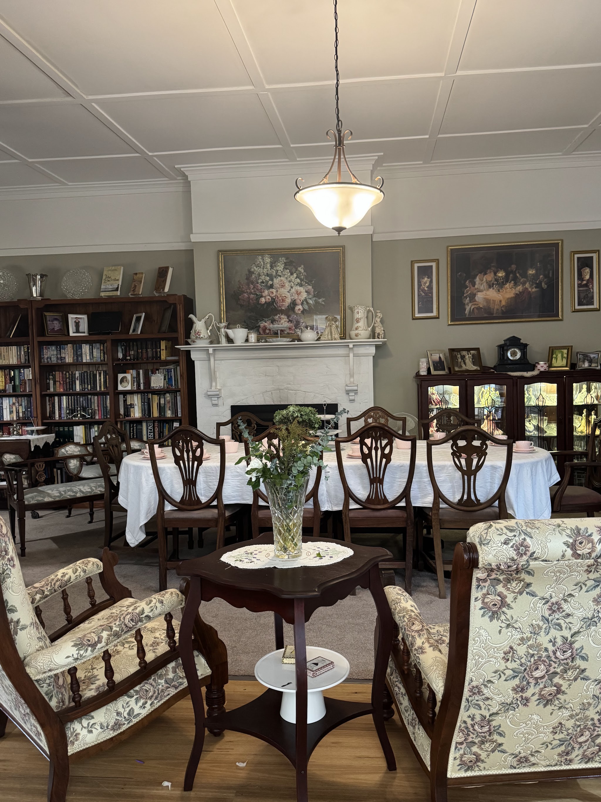 The parlour dining room with a long table set for a group, antique chairs, fireplace and bookshelves